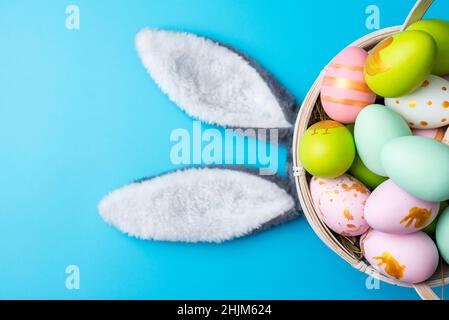 A basket of Easter eggs with bunny ears on blue background. Top view. Easter greeting card. Stock Photo
