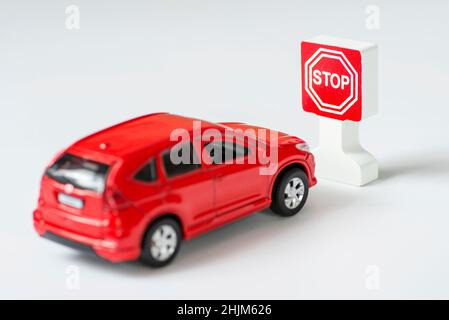 A car and stop road sign on a white background. Toy car parked next to a toy stop sign. Traffic Laws. Stock Photo