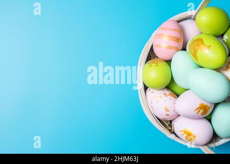 Easter basket filled with painted Easter Eggs over a blue background. Colorful painted easter eggs in basket on blue background. Stock Photo