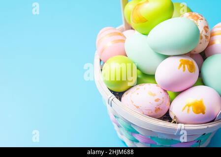 Easter basket filled with painted Easter Eggs over a blue background. Colorful painted easter eggs in basket on blue background. Stock Photo