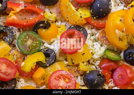 detail of an unbaked homemade pizza top with peppers tomato olives cheese and herbs ready to bake Stock Photo