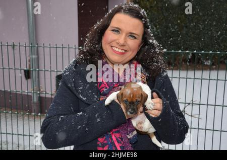 happy woman holds a three-week-old Jack Russell Terrier puppy in her arms. In winter with snowfall. Stock Photo