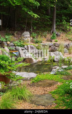 Deschampsia cespitosa - Tufted Hair Grass next to flagstone path leading to pond with Acorus calamus ‘variegatus' - Variegated Sweet Flag, Pontederia. Stock Photo