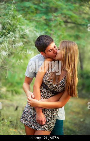 handsome young man kisses an underage girl in park while walking in nature. couple spends time together on Valentine's Day Stock Photo