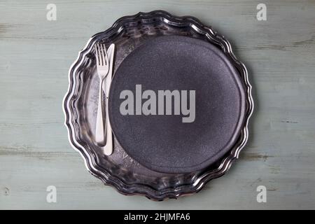 Dark plate with cutlery on a vintage shiny metal tray on a light wooden table Stock Photo