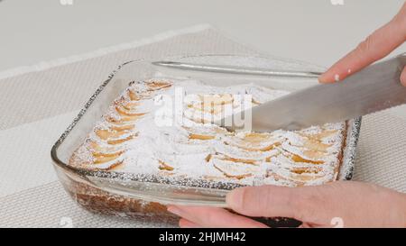 Apple cake with biscuit base recipe. Fresh baked cake in a glass bowl. Woman serving cake