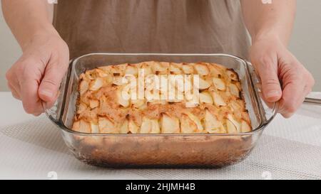 Fresh baked apple cake with biscuit base close up on kitchen table, just from the oven, woman hands