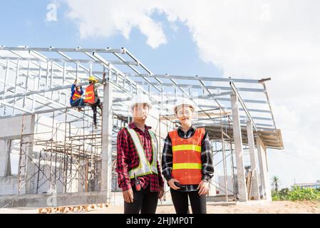 Architect and client standing at home building construction site. Portrait Asian engineer foreman worker man and woman in hardhat posing on building, Stock Photo