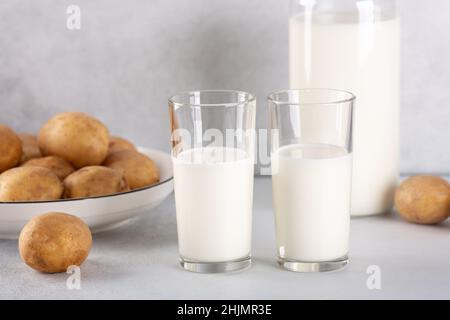 Vegan plant based milk in two transparent glasses. Alternative potato milk and potato tubers on gray table Stock Photo