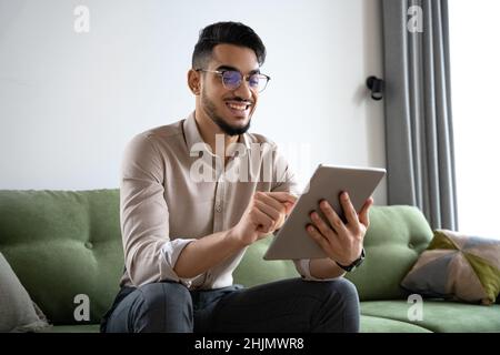 Young man using digital tablet computer sitting on sofa at home office Stock Photo