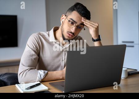 Headshot thoughtful indian businessman in eyewear looking at laptop screen Stock Photo
