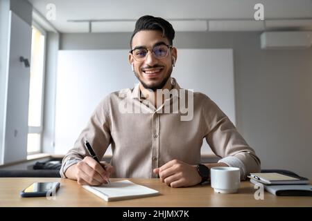 Smiling hindu man sitting at table holding pen for notes looking at camera Stock Photo
