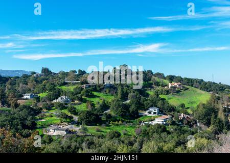 Upscale hillside homes in suburban residential neighborhood on green hills under blue sky Stock Photo