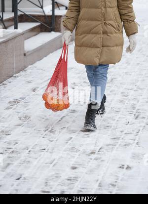 Happy woman carry reusable bag with oranges from the shop. Walking outdoors in winter. Festive atmosphere. Ecofriendly fruits shopping Zero waste Stock Photo