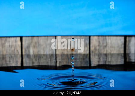 Circles and splash on water from raindrops on background an old fence and blue sky Stock Photo