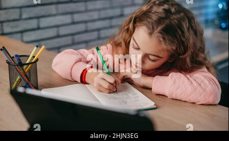 Schoolgirl doing her homework using digital tablet at home. Distance education. Girl studying online. Modern online education. Stock Photo