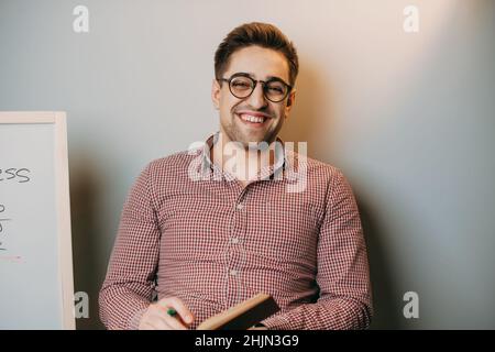 Half length portrait of a teacher in eyewear looking at camera while holding literature book in hand for making research of information. Smiling face. Stock Photo