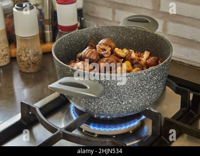 Chicken legs baked with chestnuts and mushrooms in saucepan on gas stove. French gourmet cuisine Stock Photo