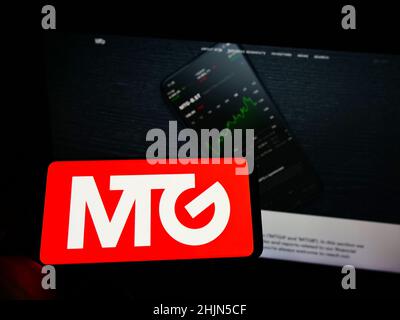 Person holding cellphone with logo of Swedish company Modern Times Group AB (MTG) on screen in front of business webpage. Focus on phone display. Stock Photo