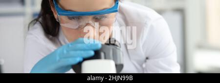 Young woman scientist with glasses looks through microscope closeup Stock Photo