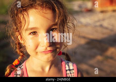 Funny summer portrait of a 5-year-old little girl in the orange sunset light and with disheveled hair. A real childhood, a sweet and sincere child. Li Stock Photo