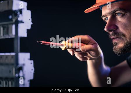 A male electrician works in a switchboard with an electrical connecting cable. Stock Photo