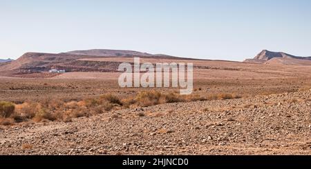 panorama of the bottom of the Maktesh Ramon crater showing one solitary campsite with sparse vegetation in the foreground and a clear blue sky in the Stock Photo