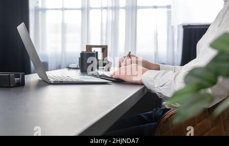 Man hands writing in diary. Businessman sitting at table in office or at home and working on laptop or studying online. Online work and education concept. High quality photo Stock Photo