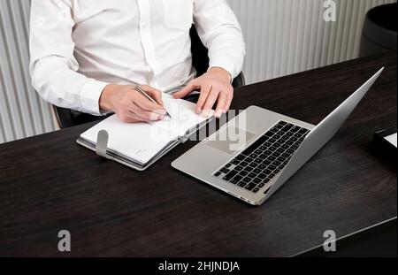 Man taking notes in planner. Businessman sitting at desk and working or studying on laptop. Online education or using computer technology in work concept. High quality photo Stock Photo