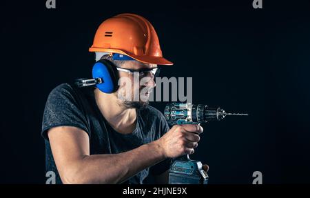 A young man in overalls protective helmet hard hat hold electric drill. Stock Photo