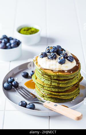 Matcha tea green pancakes with coconut cream, blueberries and maple syrup, white background. Vegan dessert concept. Stock Photo