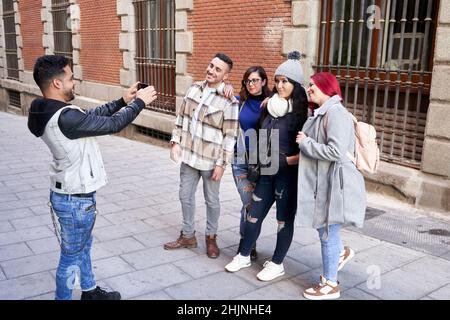 Latino man taking a picture with his smart phone of his group of friends on a city street.  Stock Photo