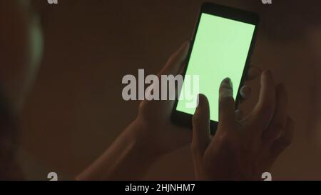 Close-up of a woman tapping on a green phone screen. Stock. Woman runs fingers over green screen of phone in fascination. Woman taps green screen of p Stock Photo