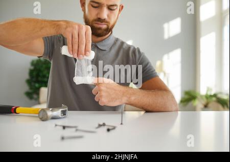 Man wrapping his finger with a piece of gauze bandage after he hits it with a hammer Stock Photo