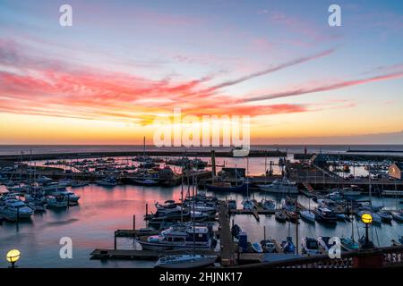 Colourful dawn sky over the English Channel and Ramsgate Royal Harbour in Kent, England. Harbour filled with boats and a yachting marina with an overhead sky of red pink clouds and yellow sky changing to blue higher up. Stock Photo