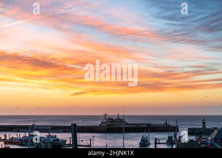 Colourful dawn sky over the English Channel and Ramsgate Royal Harbour in Kent, England. Harbour entrance with a small lighthouse and overhead, sky of red pink clouds and yellow sky changing to blue higher up. Stock Photo