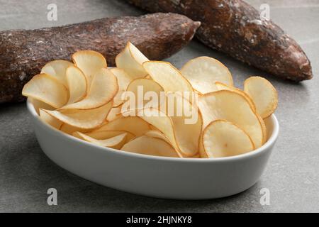 Bowl with deep fried cassava chips close up and waxed cassave tuber in the background Stock Photo