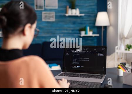 Student writing code on laptop in home office. Freelance programmer developing software. Freelancer coder working remote typing on keyboard. Software tester debugging looking for errors. Stock Photo