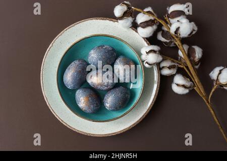 Easter concept of coloring eggs in hibiscus, eco diy. Brown background and turquoise plate. Top view, cotton plant. Stock Photo