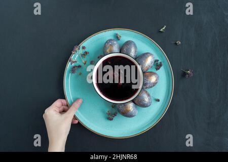 Easter concept of coloring eggs in hibiscus, eco diy. Top view, black background and turquoise plate. Stock Photo