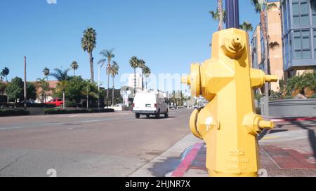 Yellow fire hydrant extinguisher on pavement of San Diego city street, California fire department, USA. Cars on road by walkway. Infrastructure for firefighters on sidewalk in United States. Low angle Stock Photo