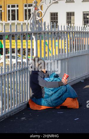 A beggar on the bridge, a homeless young man sitting on the The Penny Ha'penny Bridge begging for money, streets photography, Dublin, Ireland Stock Photo