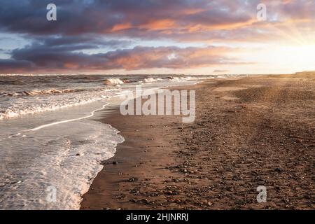 Beautiful breaking waves on Norfolk sandy beach at Burnham Overy Staithe during sunrise in Winter. Stock Photo