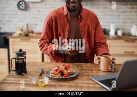 Cropped portrait of black young man using smartphone while enjoying breakfast at home kitchen, copy space Stock Photo