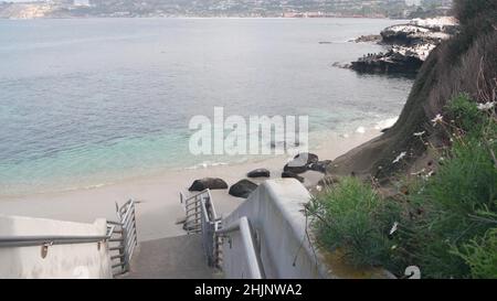 Beach access, stairs to crystal blue azure transparent calm ocean, La Jolla cove, California coast, USA. Turquoise clear sea waves. Water surface and sand, tropical paradise lagoon, summer vacations. Stock Photo