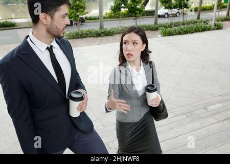Serious business colleagues walking outdoors, drinking morning coffee and discussing work Stock Photo