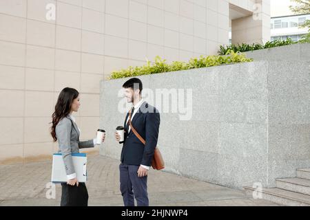 Business colleagues standing outdoors, drinking coffee and discussing news and ideas Stock Photo