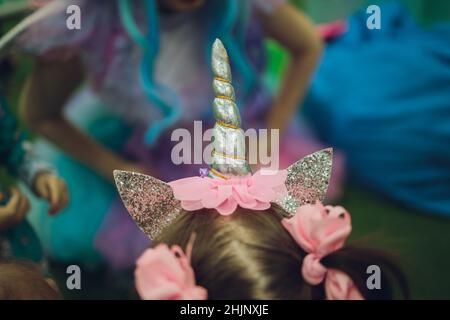 little girl wearing unicorn headband with pink background. Portrait of cute smiling child with unicorn horn and ears in front bright pink wall. Lovely Stock Photo