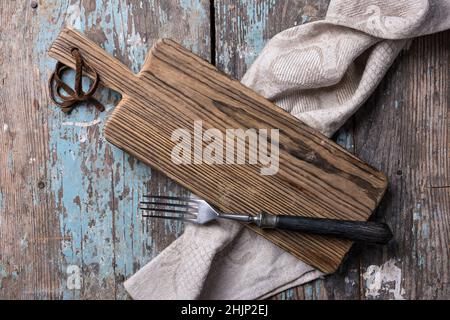 Top view of rustic cutting board, fork and folded linen serviette on blue grunge and shabby wooden background Stock Photo