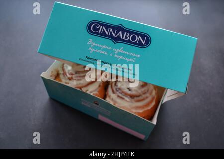 Moscow, Russia, November 2019: Two classic rolls with cinnamon and cheese cream on top in an open branded box of the sign Cinnamon on black background Stock Photo